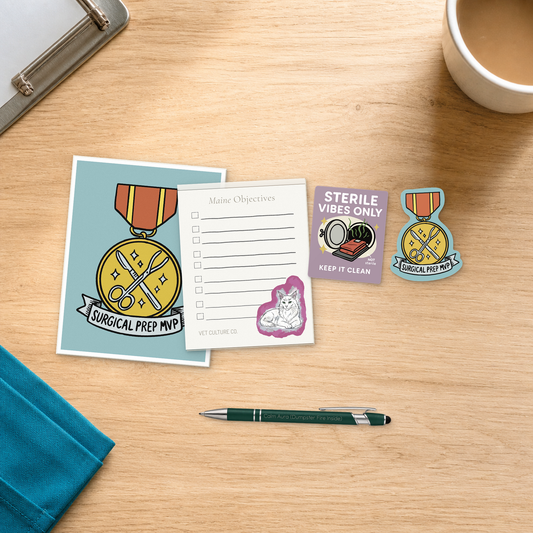 Surgery Suite Sanity Kit with a Surgical Prep MVP card, notepad, engraved pen, and two stickers, arranged on a light oak desktop for veterinary professionals