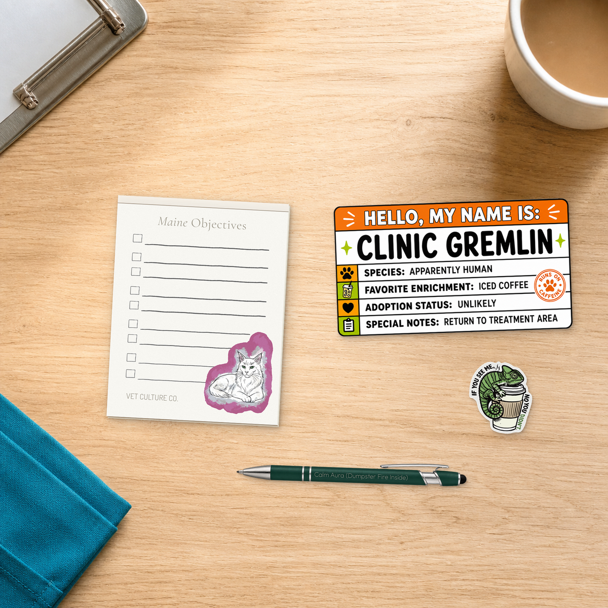 Clinic Gremlin Survival Kit with a notepad, engraved pen, large name-tag sticker, and chameleon sticker, arranged on a light oak desktop for veterinary professionals