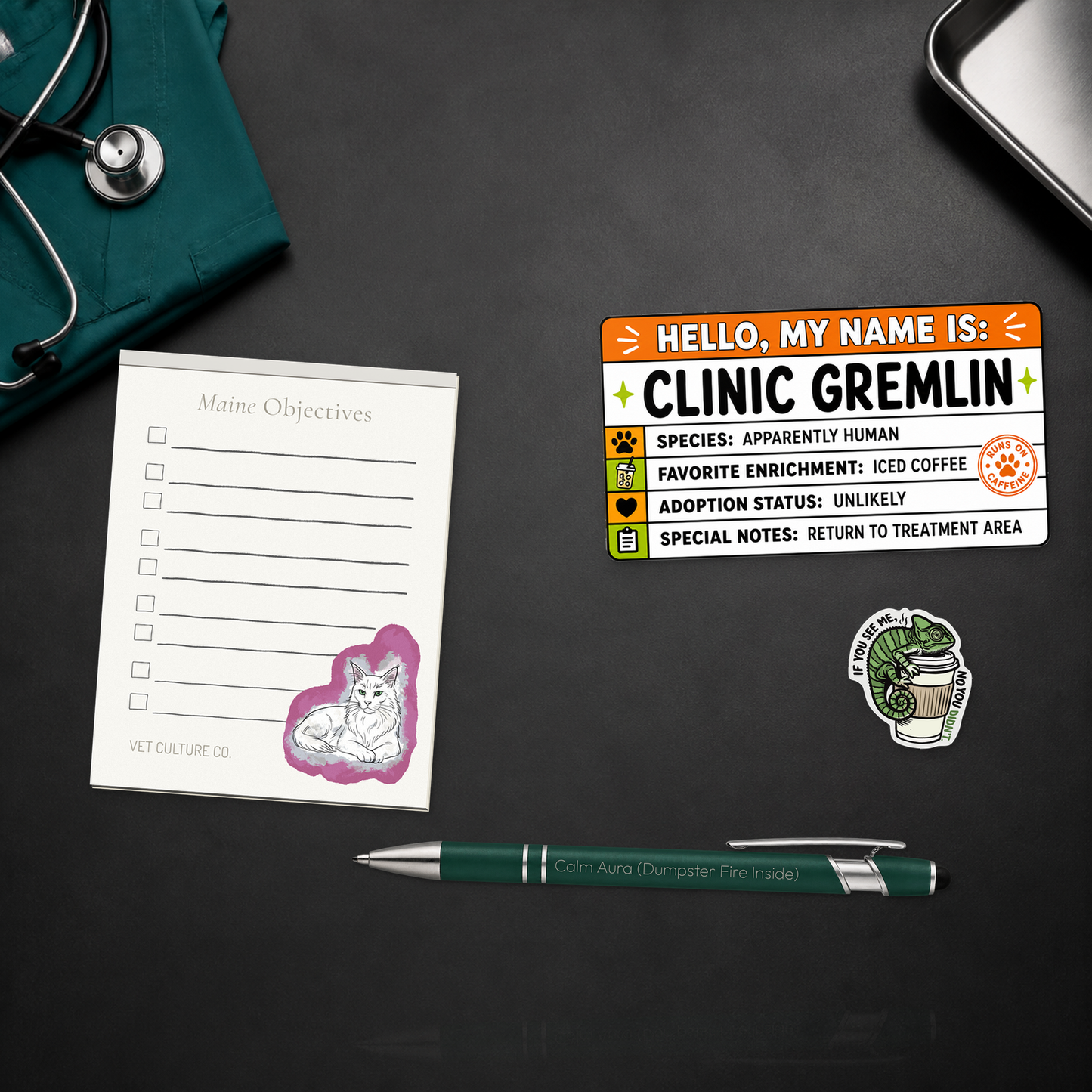 Clinic Gremlin Survival Kit with a notepad, engraved pen, large name-tag sticker, and chameleon sticker, shown in a close material-detail scene for veterinary professionals