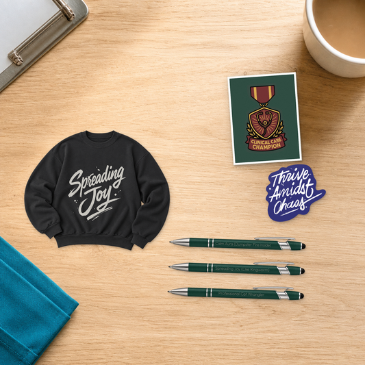 Spreading Joy Uniform Upgrade with a black cropped crewneck, Clinical Care Champion card, three engraved pens, and a Thrive Amidst Chaos sticker, arranged on a light oak desktop for veterinary professionals