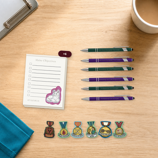 Desk Drop Six-Pack veterinary team bundle with six notepads, six engraved pens, and six award stickers, arranged on a light oak desktop for veterinary professionals